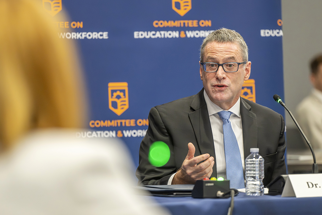Man speaking behind a table to people at a committee