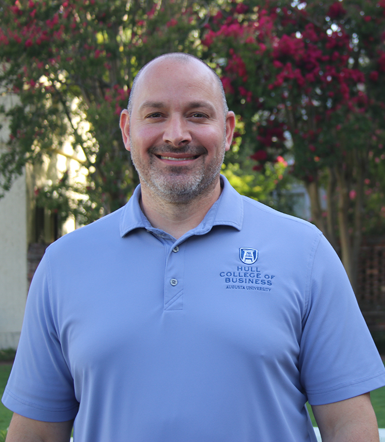 Man in a blue shirt standing and smiling for a photo