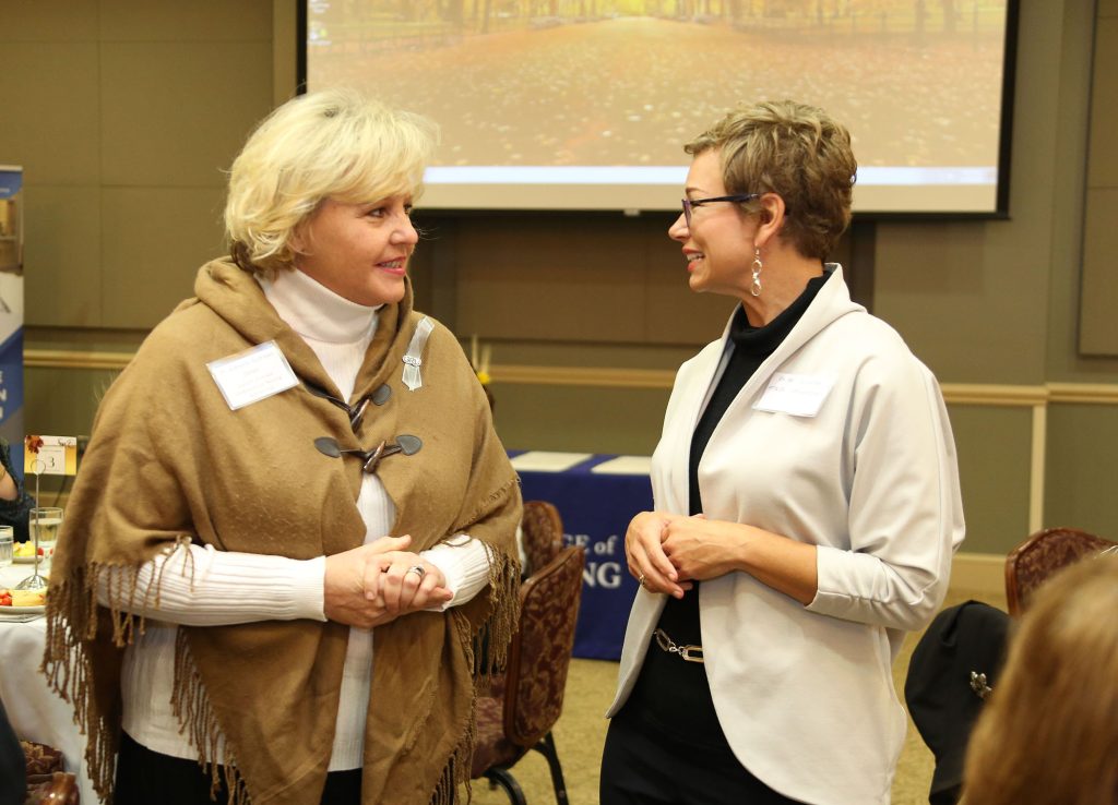 Two women speak to each other in a conference room, surrounded by chairs.