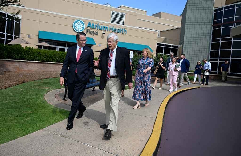 Two men in business dress walk on a sidewalk with a line of people also walking behind them
