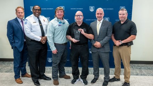 six men stand together smiling with one holding an award