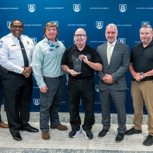 six men stand together smiling with one holding an award