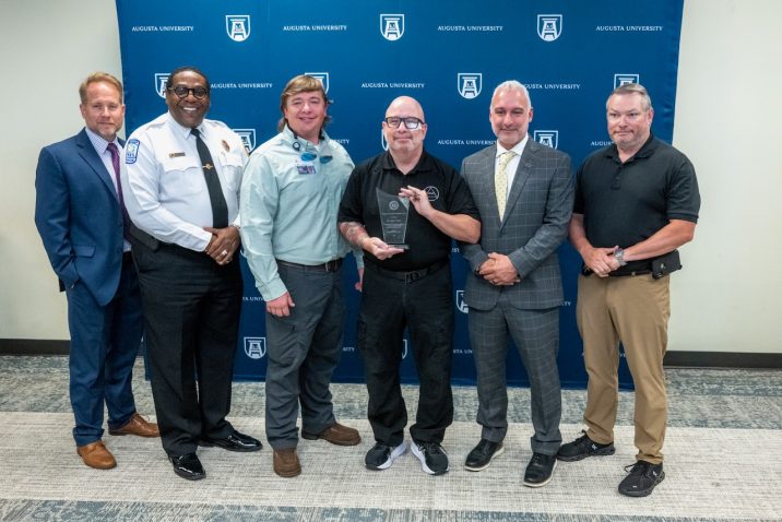 six men stand together smiling with one holding an award
