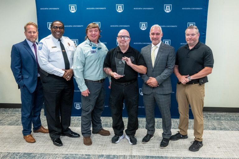 six men stand together smiling with one holding an award