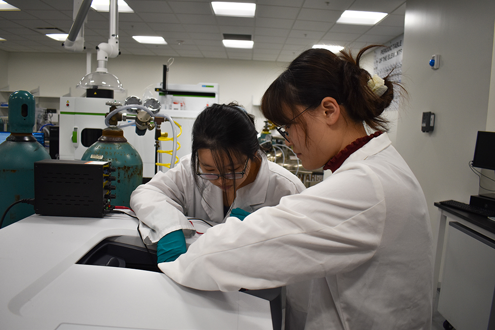 two women wearing lab coats working on a machine