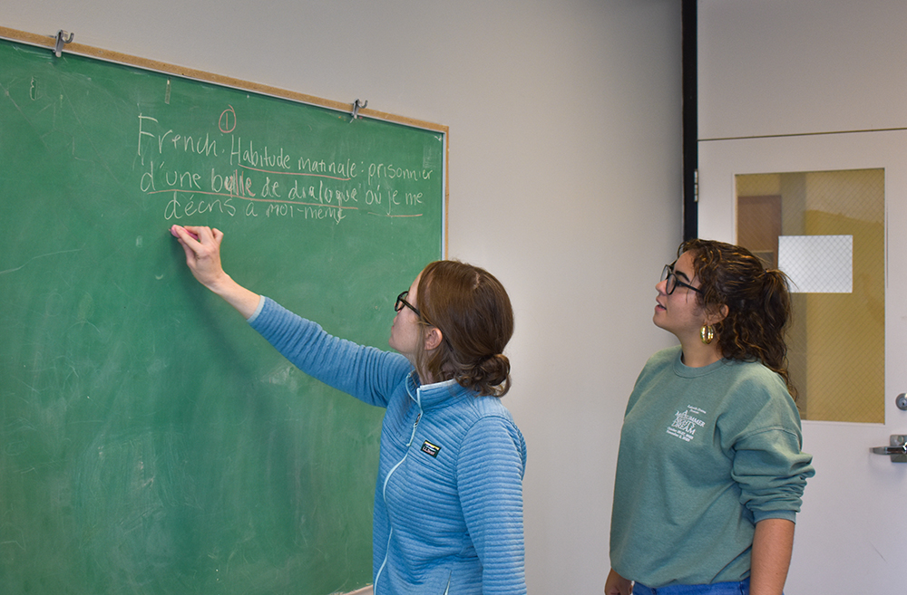 woman writing on a chalkboard and another woman looking at the board