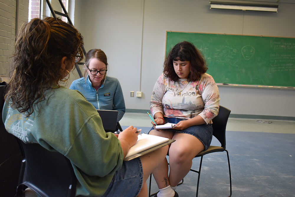 three women sitting together and working on a computer.