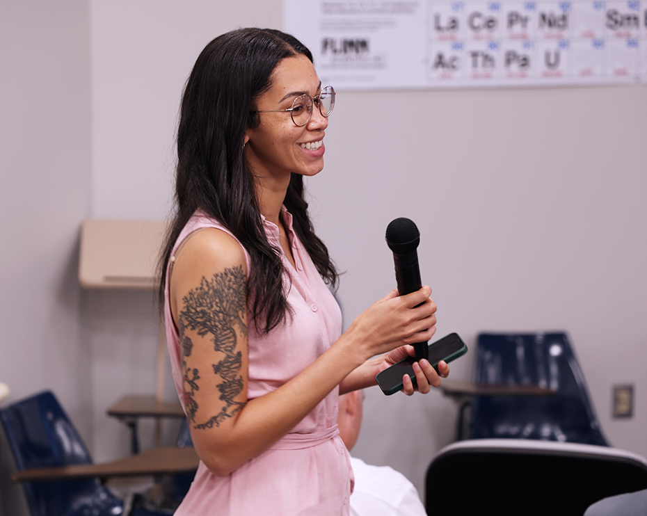 A woman speaks into a microphone in an auditorium.
