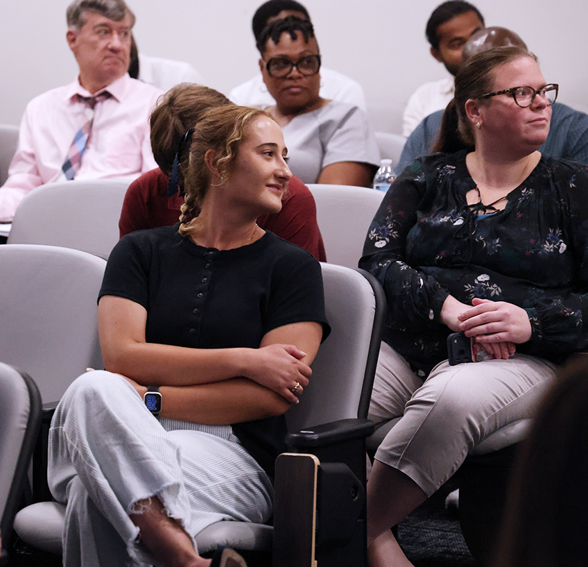 Men and woman sit in chairs in an auditorium and listen to a speaker.
