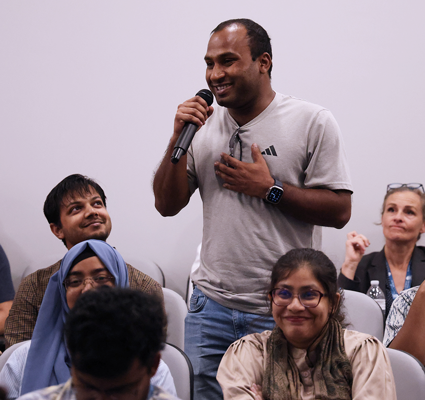 A man speaks into a microphone in an auditorium.
