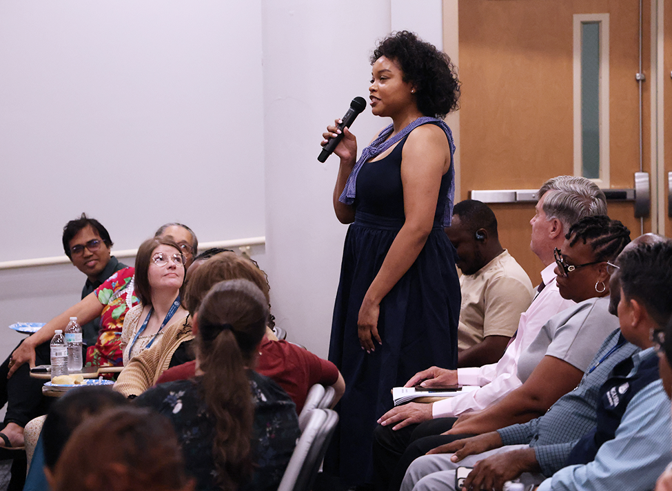 A woman speaks into a microphone in an auditorium.