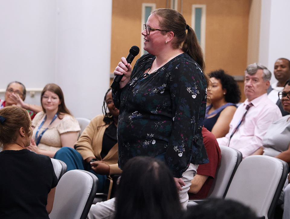 A woman speaks into a microphone in an auditorium.
