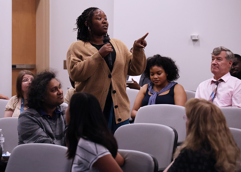 A woman speaks into a microphone in an auditorium.