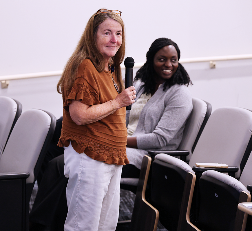 A woman speaks into a microphone in an auditorium.