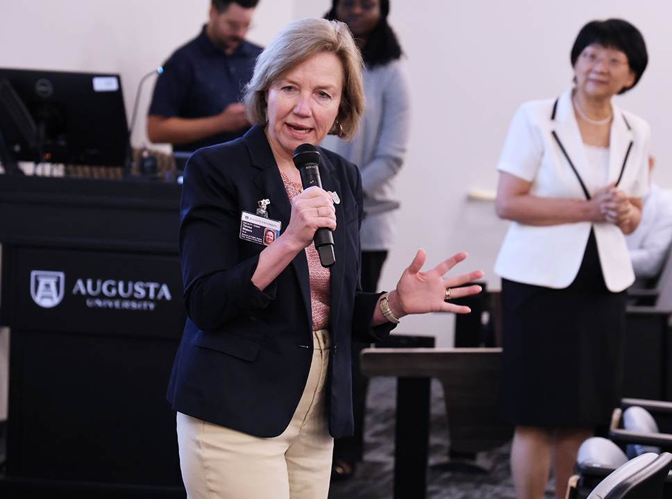 A woman speaks into a microphone in an auditorium.