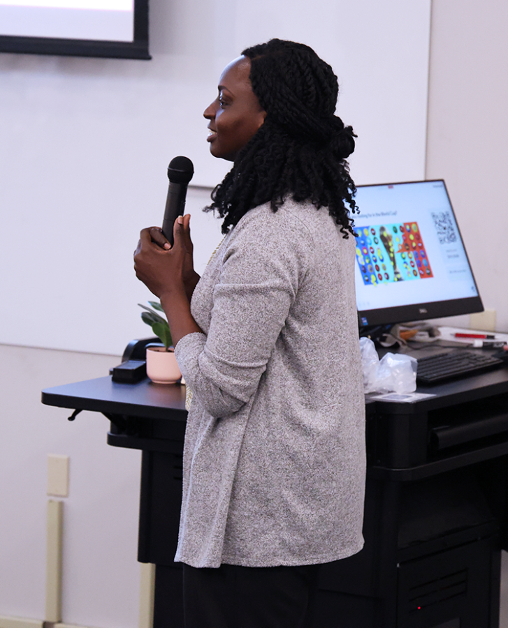 A woman speaks into a microphone in an auditorium.