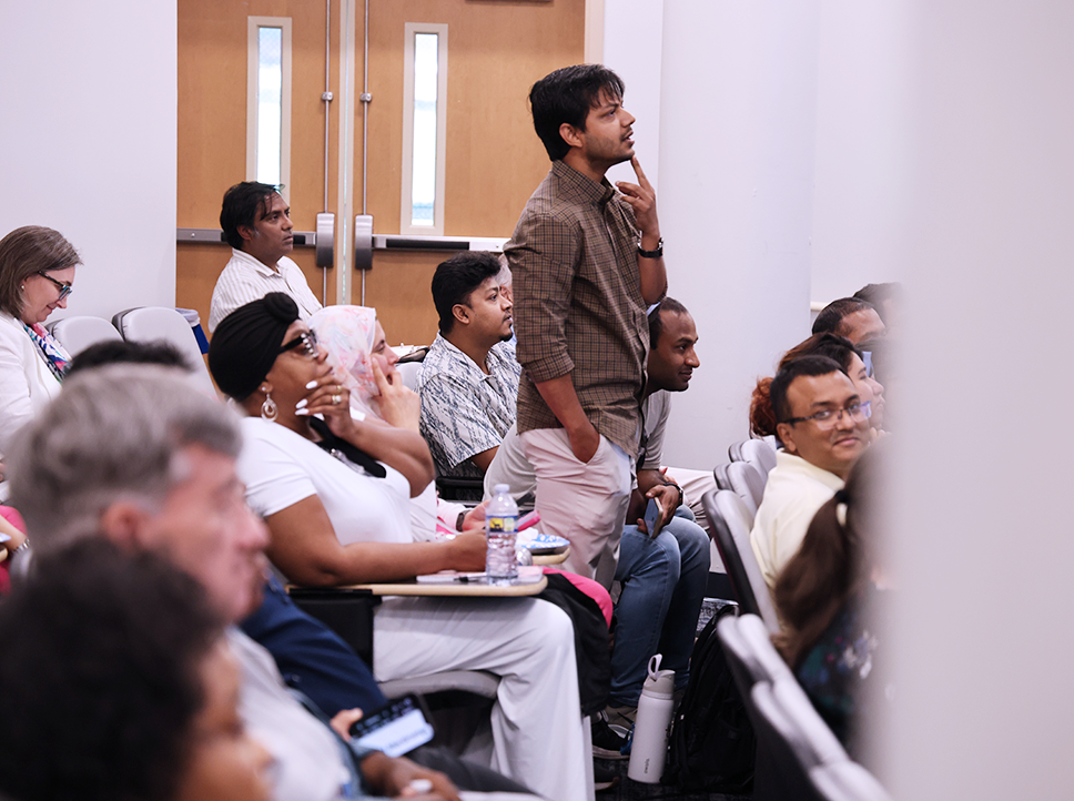 A man stands in a row in an auditorium and looks pensively at the front of the room.