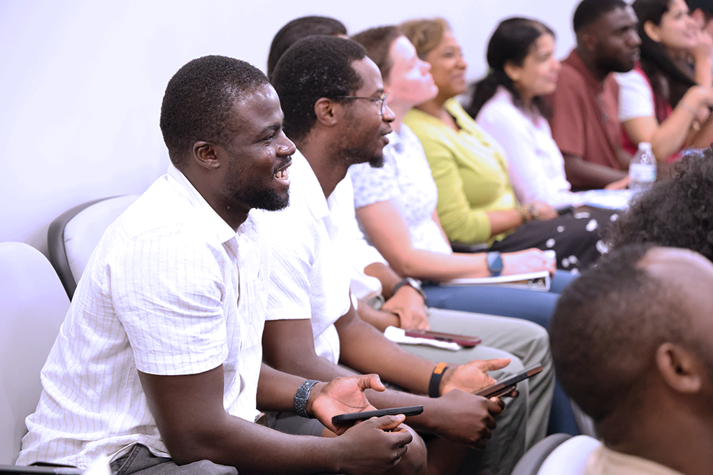 A row of people sit in seats in an auditorium and smile.