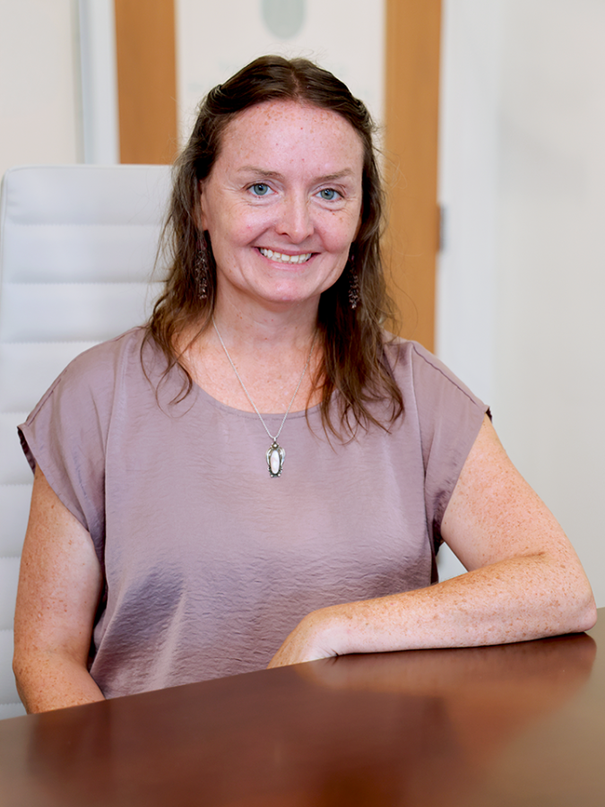 A woman sits at a table and smiles at the camera.