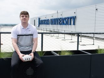Man in setting on raling in front of AU logo with meta goggles