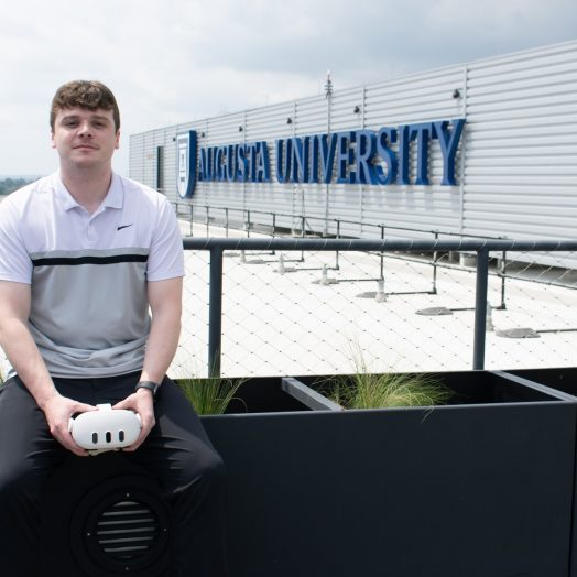 Man in setting on raling in front of AU logo with meta goggles