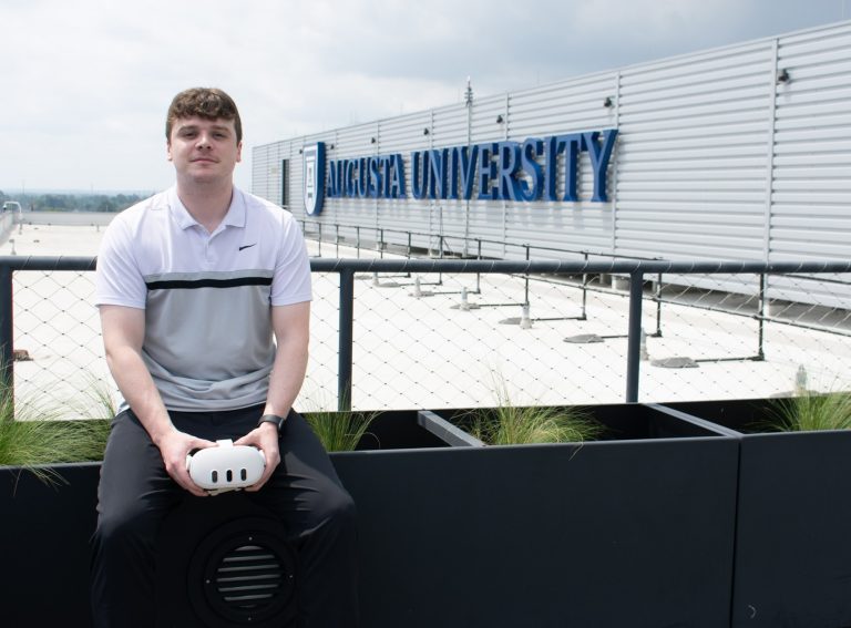 Man in setting on raling in front of AU logo with meta goggles