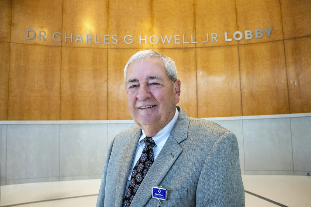 man in suit stands in front of his name on wall