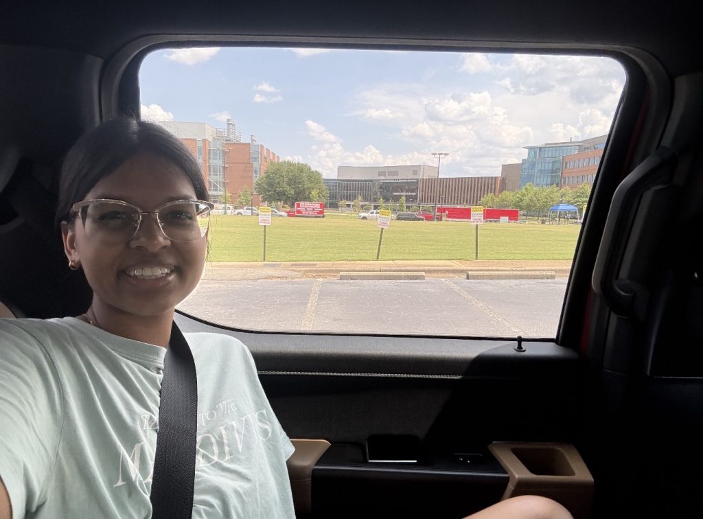 A college-a women sitting inside a vehicle while smiling. 