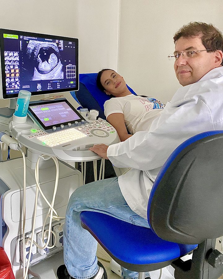 Man sitting at an ultrasound machine with a woman sitting on a table next to him.