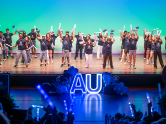 A group of young people on a stage holding pom-poms and glowsticks.