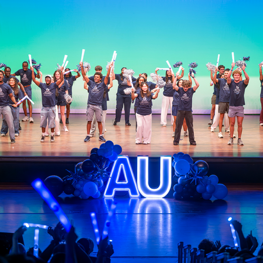 A group of young people on a stage holding pom-poms and glowsticks.