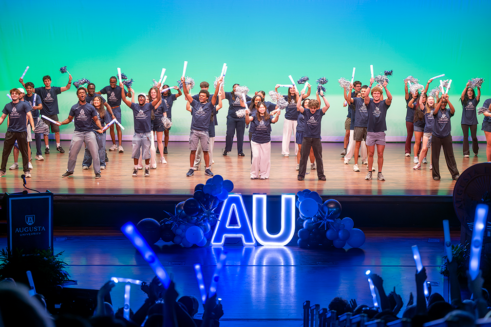 A group of young people on a stage holding pom-poms and glowsticks.
