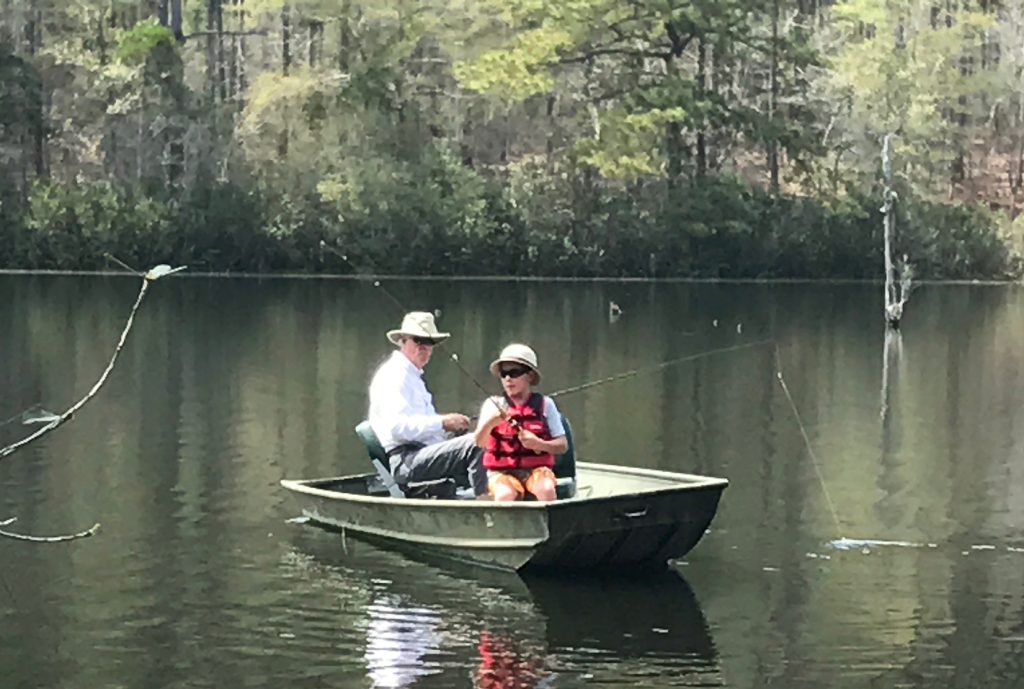 man and boy fishing in boat on pond