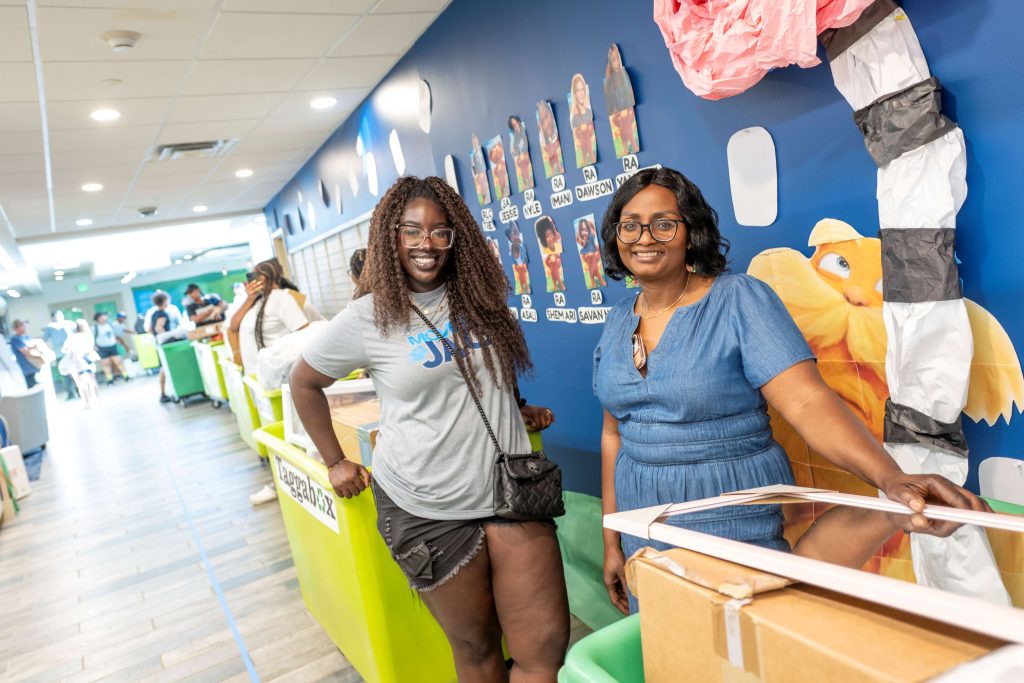 A women wearing a move-in volunteer shirt and a parent push carts indoors.