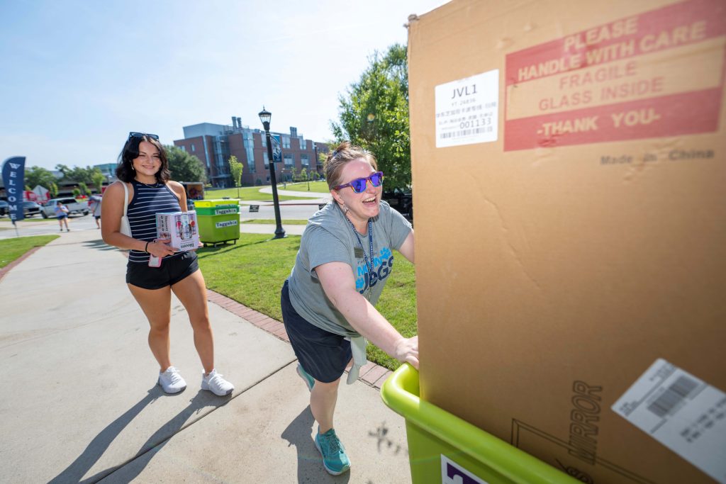One female volunteer pushes a move-in cart while a new student follows behind her.
