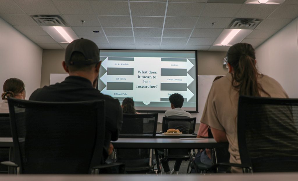 Male and female students sit in a classroom and look at a big screen 