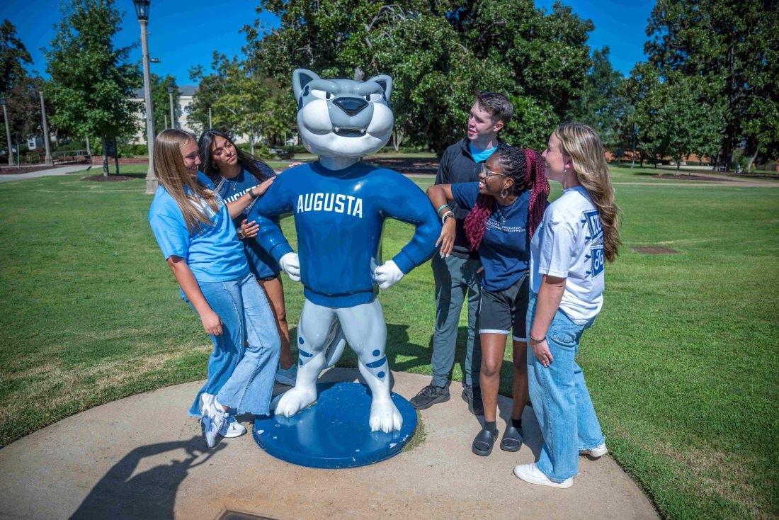 Several college-aged students surrounding the AU mascot Augustus
