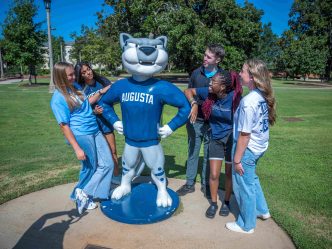 Several college-aged students surrounding the AU mascot Augustus