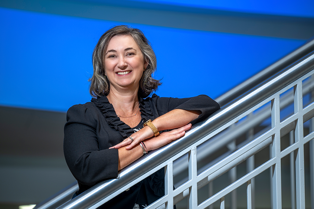 A woman smiles while resting her arms on stair railings.