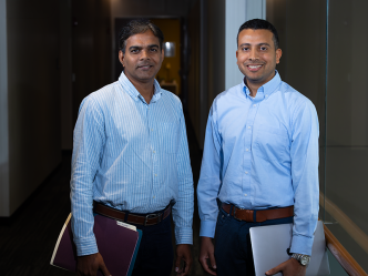 A pair of male scientists stand in a hallway of a modern research building on the campus of university.