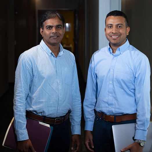 A pair of male scientists stand in a hallway of a modern research building on the campus of university.