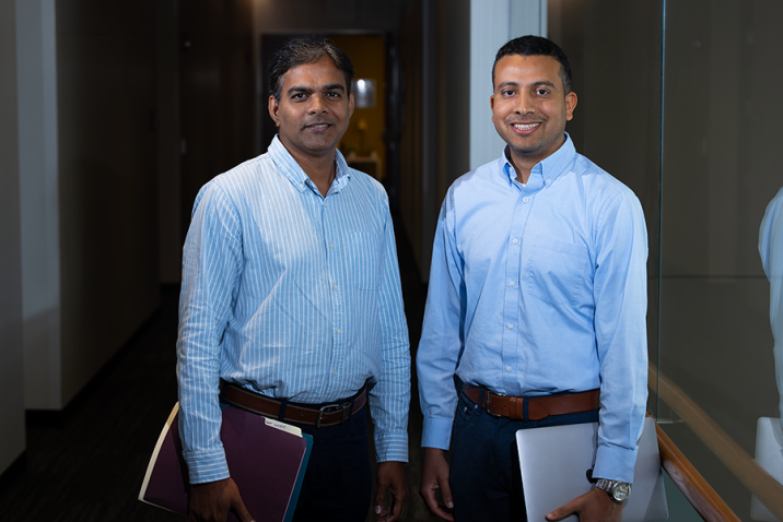 A pair of male scientists stand in a hallway of a modern research building on the campus of university.