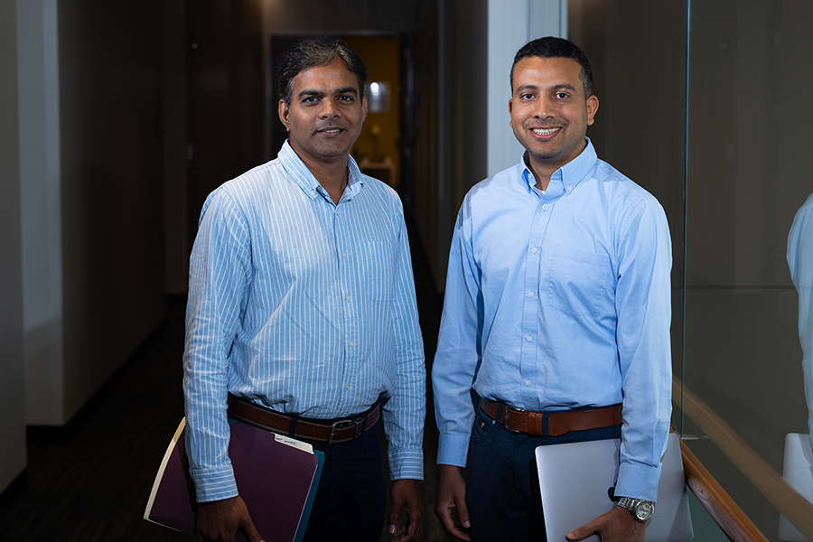 A pair of male scientists stand in a hallway of a modern research building on the campus of university.