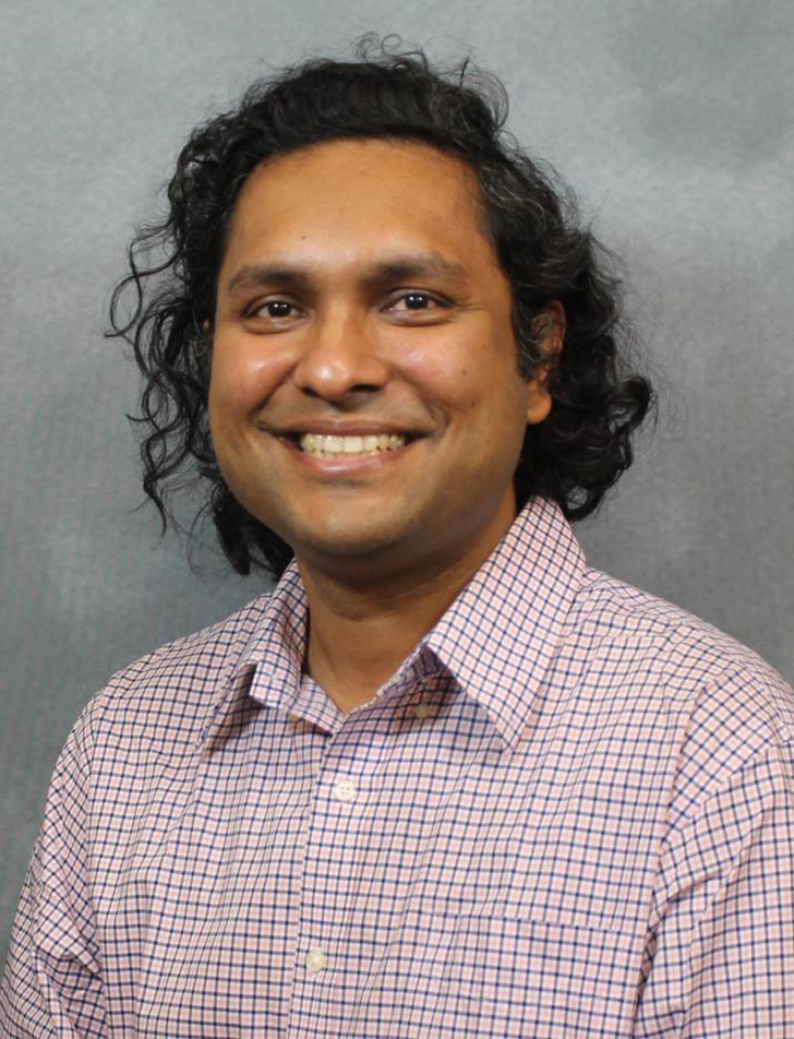 A man wearing a button down shirt smiles at the camera.