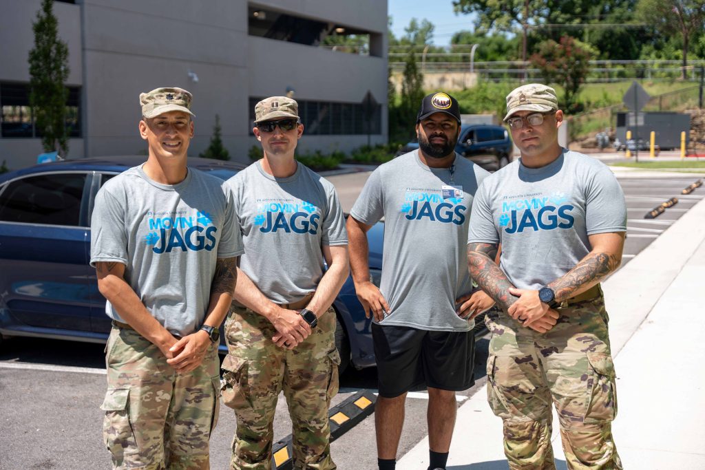 A group of men wearing move-in volunteer shirts and military camo pants gather for a photo. 