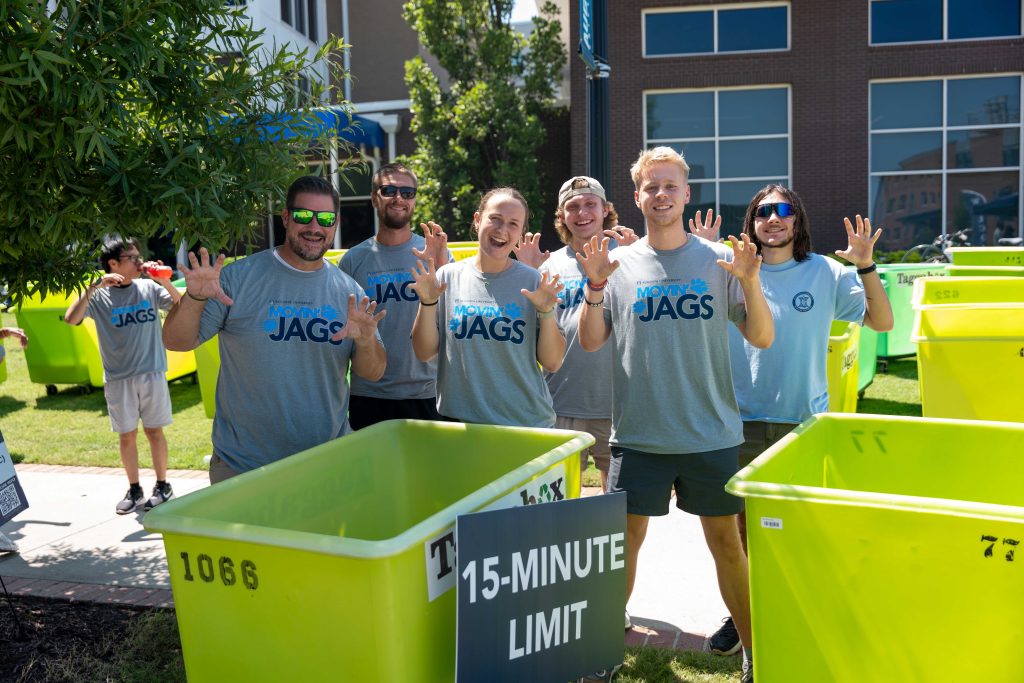 Several men and women wearing move-in shirts give a "paws up" while surrounded by move-in carts. 