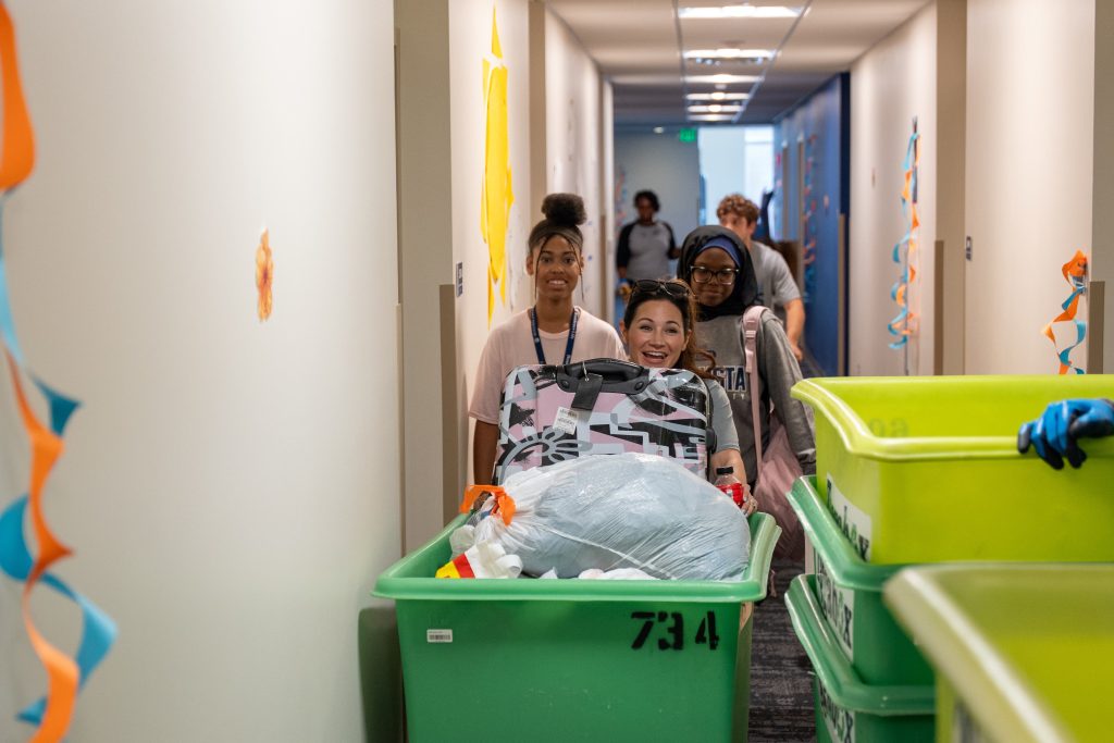 A women pushing a car down a hall smiles for a photo.