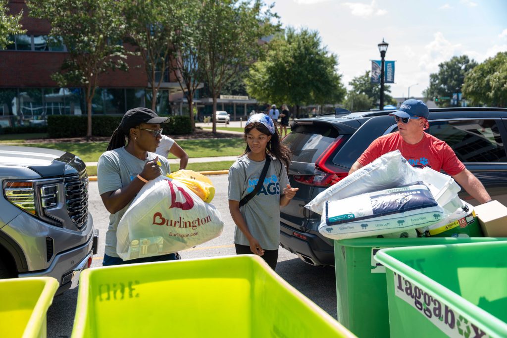 Two college-aged female volunteers with an older male volunteer help students put items into carts.