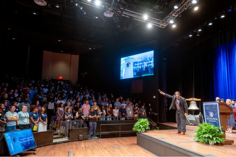 man on stage holding out the microphone to a group of people in audience