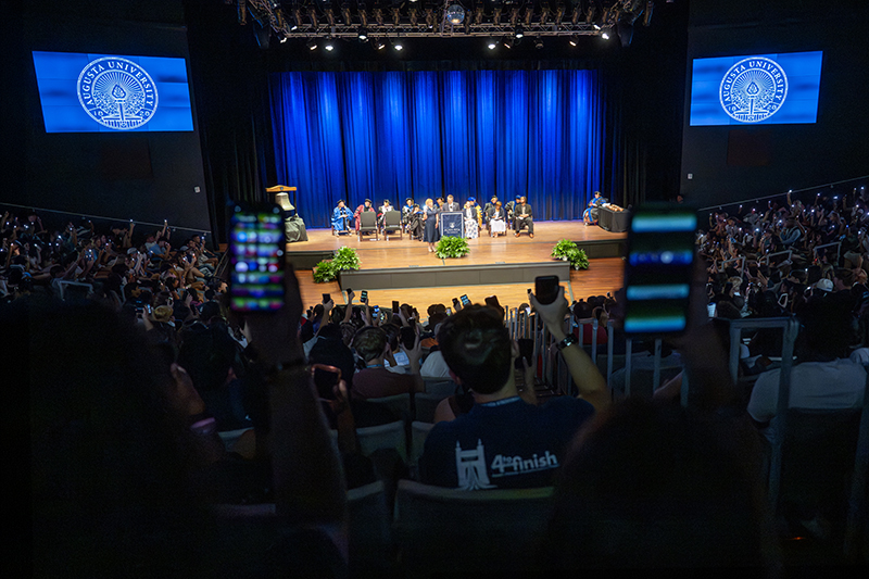 group of people seated holding up the flashlights on their phones